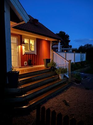 Access till altanen från trädgården. Hit kan du också köra bilen för att smidigt lasta av matkassar, väskor och dylikt. Husets fasad är upplyst kvällstid, vilket skapar en fantastiskt mysig känsla.