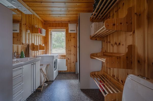 Badrum med toalett, tvättmaskin, torkskåp och pjäxhylla.