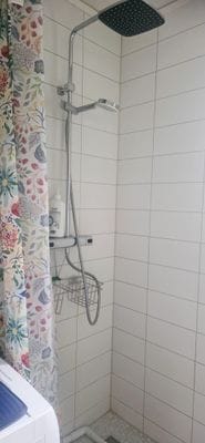 Dusch med tvättmaskin utanför duschdraperiet till vänster